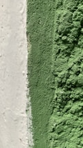 A close-up view of a textured surface with a rough, grainy green substance covering part of the area, adjacent to a smoother white section. The image captures the contrast between the smooth white surface and the coarse green coating.