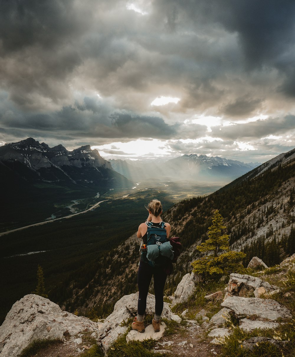 woman in black tank top and black pants standing on rocky mountain during daytime