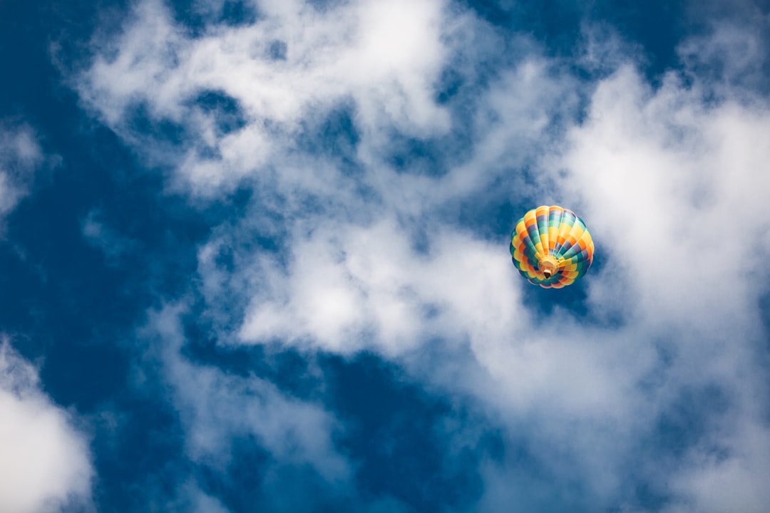 yellow green and red hot air balloon in mid air under blue and white cloudy sky