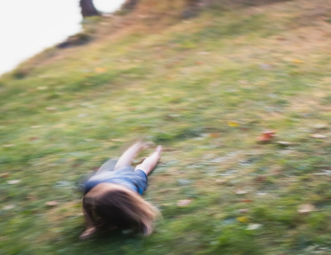 girl in white shirt lying on green grass field during daytime