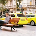 man in blue and white stripe shirt sitting on black bench near yellow taxi cab