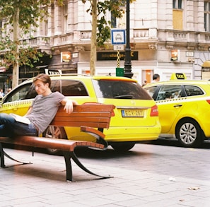 man in blue and white stripe shirt sitting on black bench near yellow taxi cab