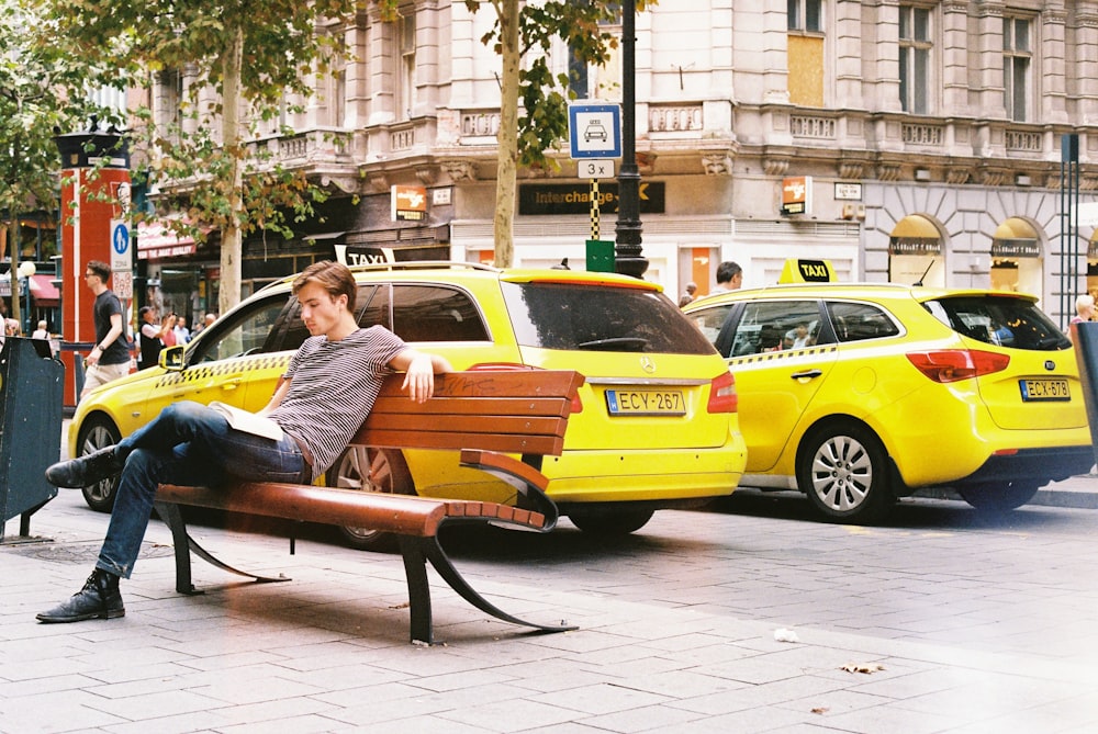 man in blue and white stripe shirt sitting on black bench near yellow taxi cab