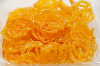 A close-up of a pile of orange, syrupy, swirled sweet treats placed in a clear plastic container.