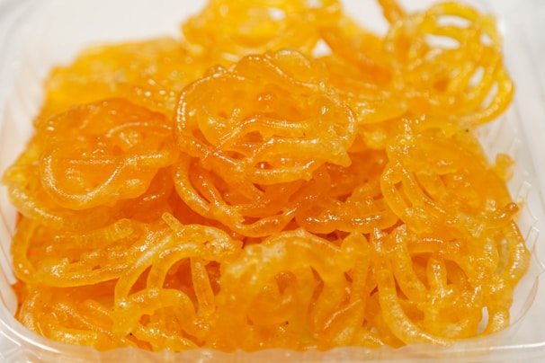 A close-up of a pile of orange, syrupy, swirled sweet treats placed in a clear plastic container.