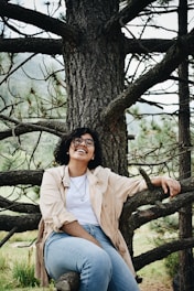 woman in white dress shirt sitting on brown tree branch during daytime