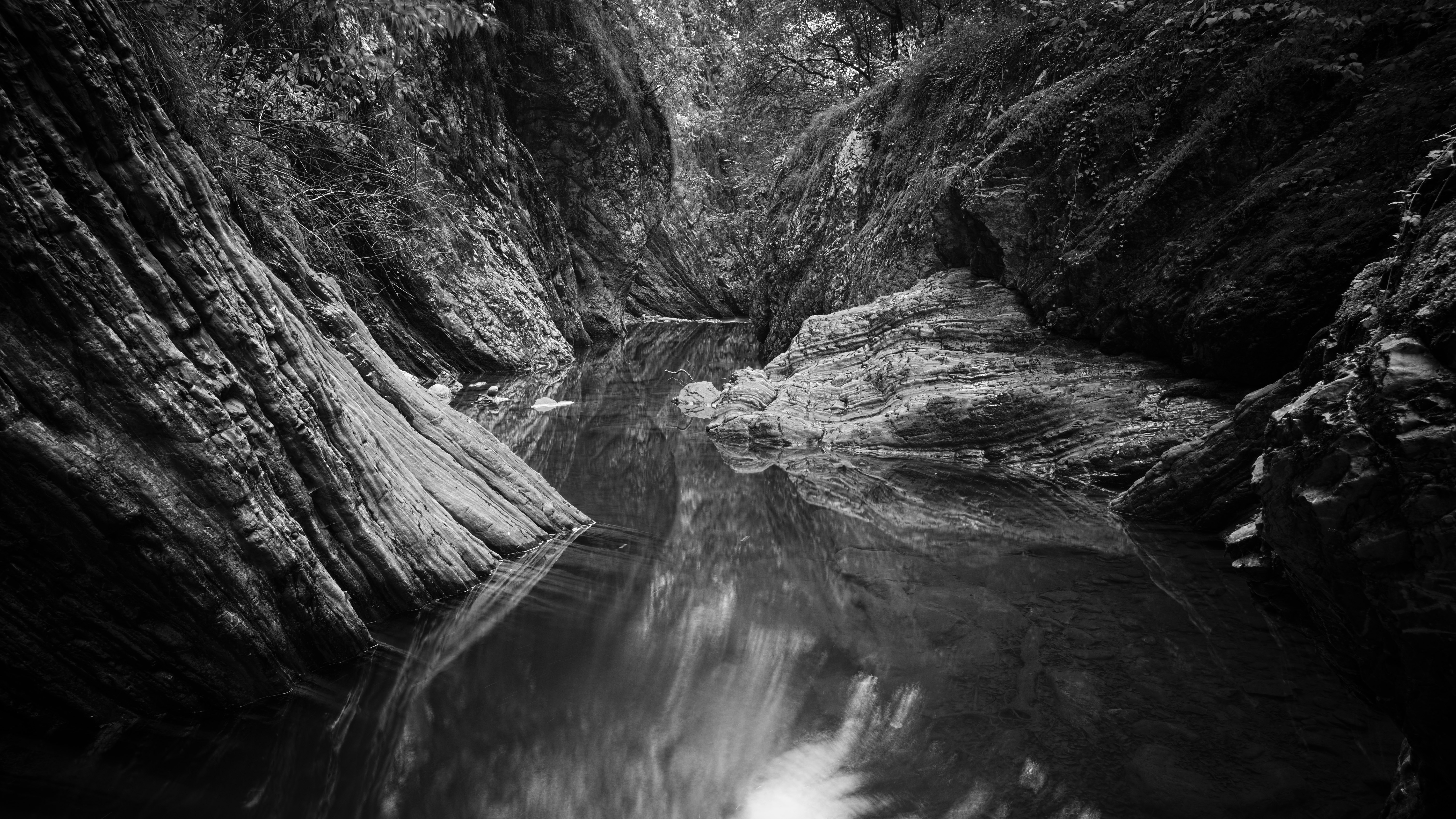 grayscale photo of river in between of rock formation