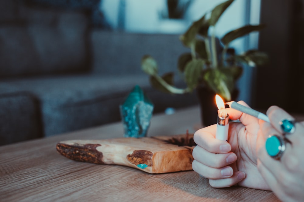 Person hält brennende Kerze auf braunem Holzschneidebrett