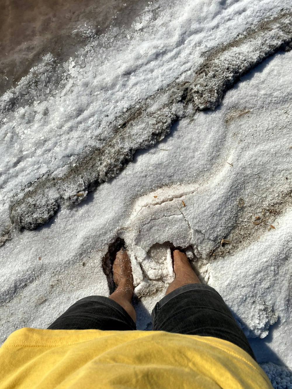 Person in schwarzen Hosen und braunen Schuhen, die tagsüber auf weißem Sand steht