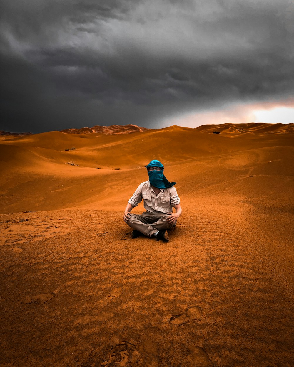 uomo in giacca grigia che si siede sulla sabbia marrone sotto il cielo nuvoloso grigio durante il giorno