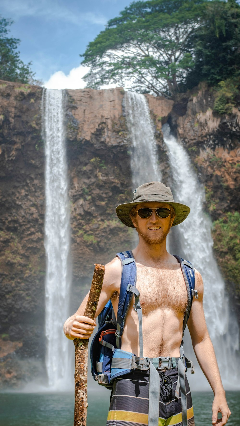 woman in blue tank top wearing brown sun hat standing near waterfalls during daytime