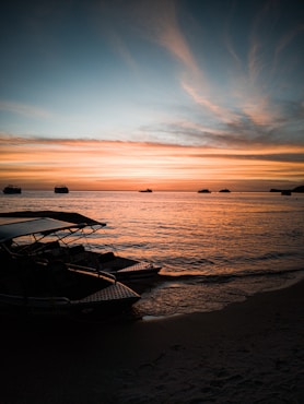 white and black boat on sea shore during sunset
