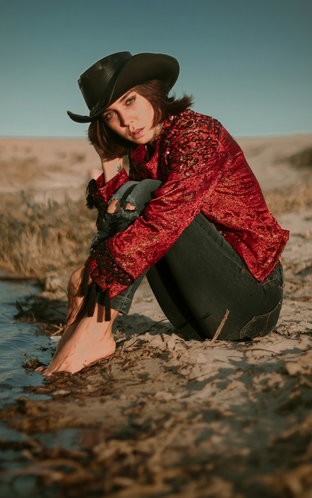 woman in red and black long sleeve dress sitting on brown rock near body of water