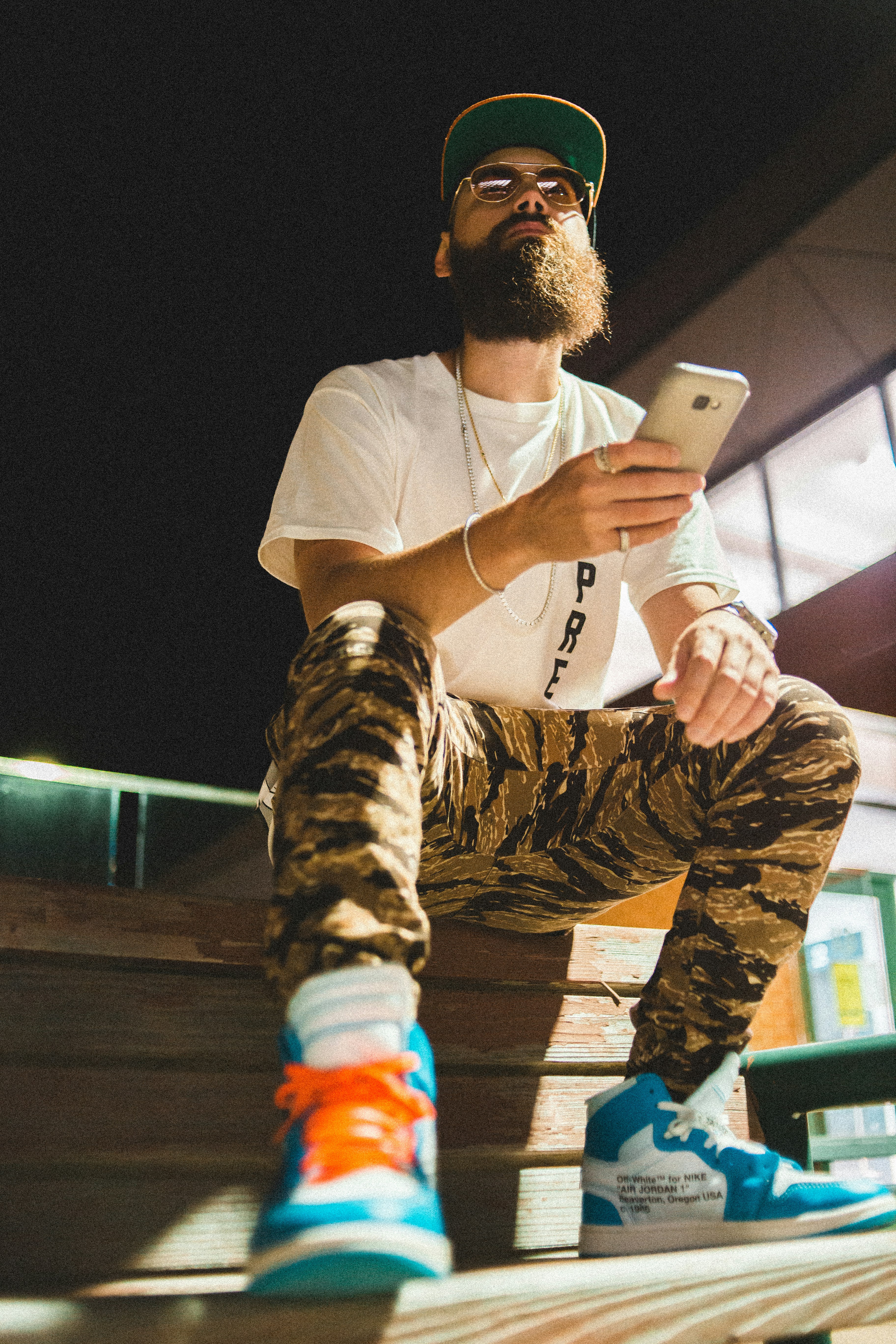 man in white crew neck t-shirt and camouflage pants holding silver iphone 6