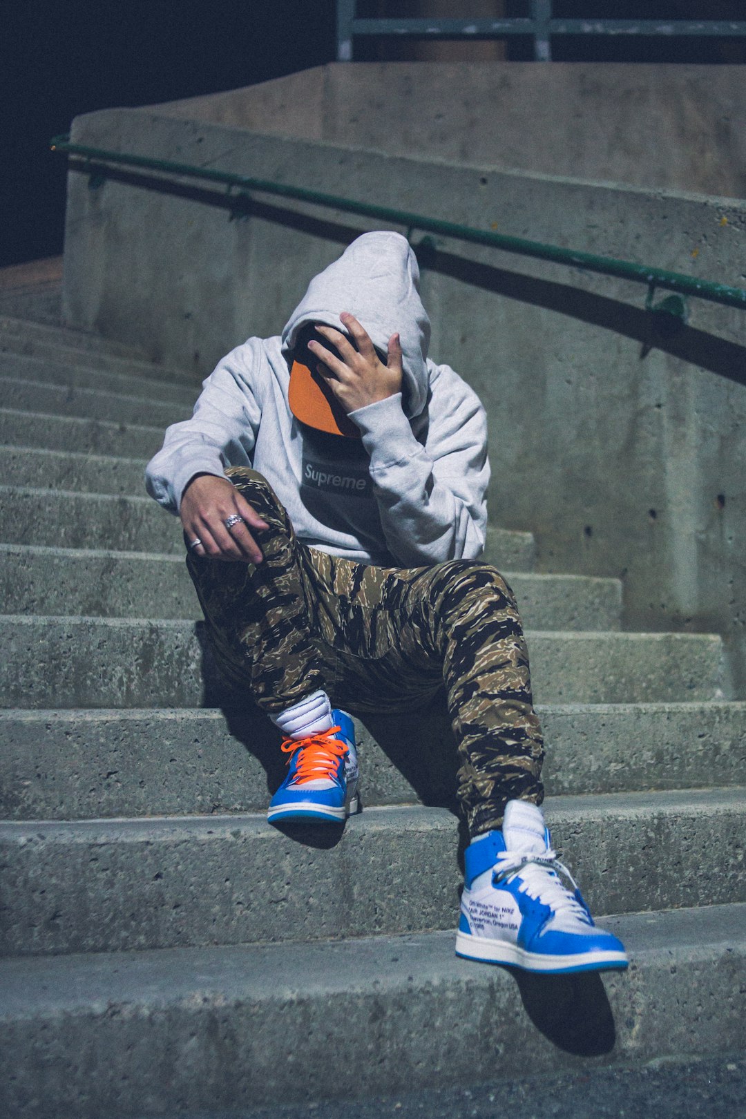man in white hoodie and black and brown pants sitting on concrete stairs