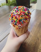 Close-up of a pastel pink scoop of strawberry ice cream in a waffle cone with sprinkles.