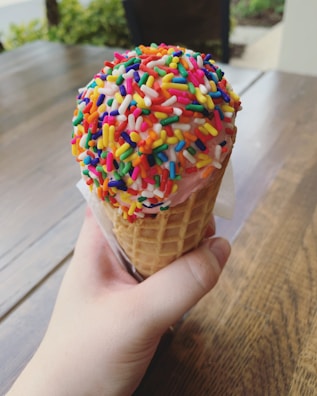 Close-up of a pastel pink scoop of strawberry ice cream in a waffle cone with sprinkles.