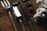 A set of garden tools including a fork, a spade, and a trowel are laid out on a rustic wooden surface. Nearby, there are pine cones and a bunch of white cotton flowers, adding a natural and earthy feel to the composition.