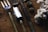 A set of garden tools including a fork, a spade, and a trowel are laid out on a rustic wooden surface. Nearby, there are pine cones and a bunch of white cotton flowers, adding a natural and earthy feel to the composition.