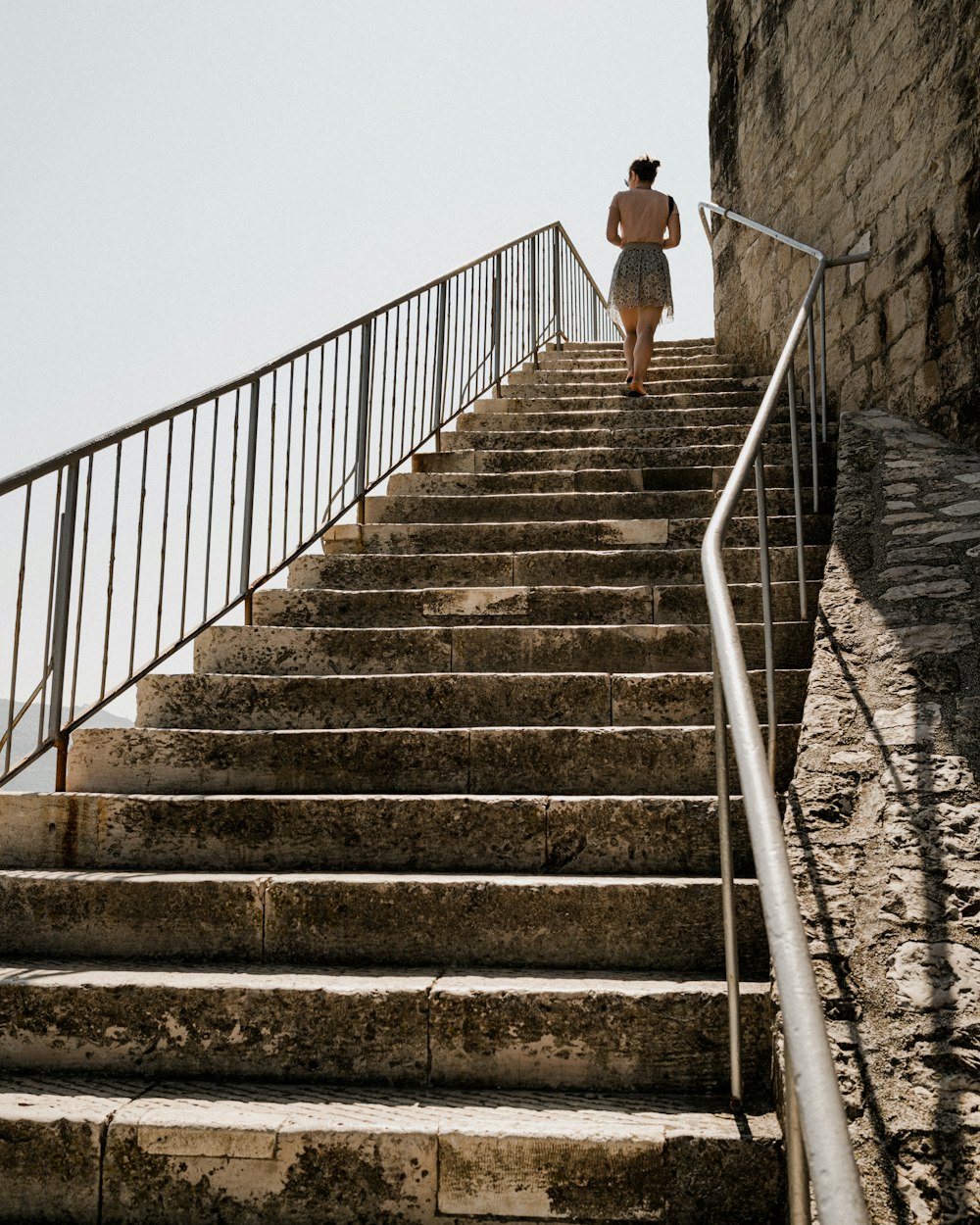 Mujer en camiseta blanca sin mangas y pantalones negros caminando por escaleras de concreto gris