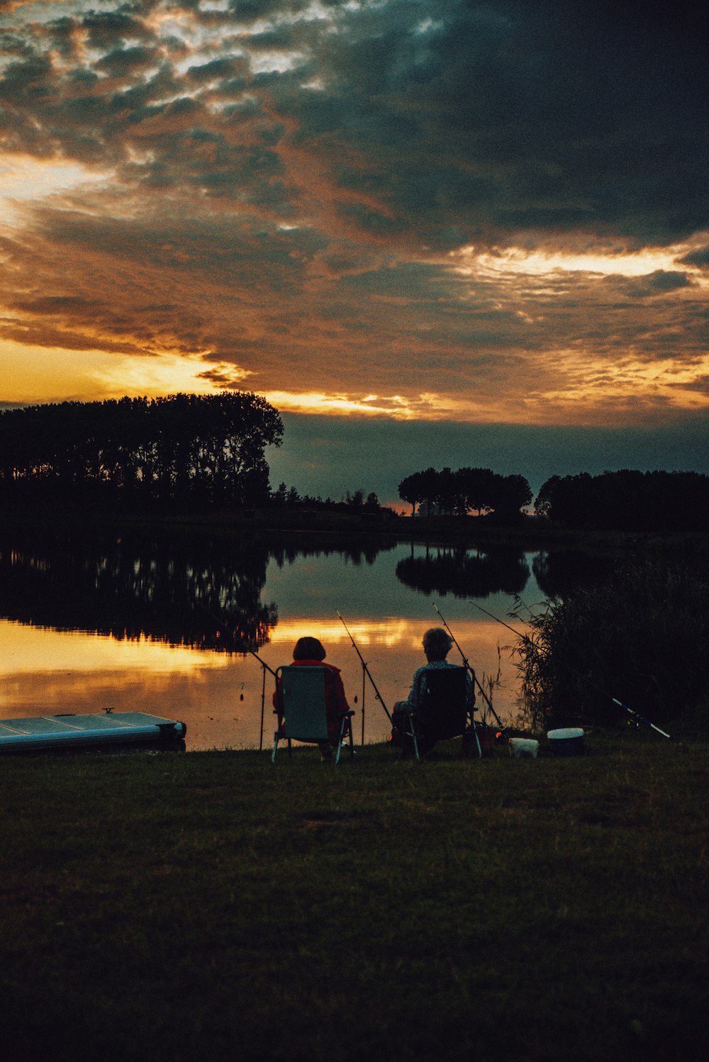 man sitting on camping chair near lake during sunset
