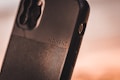 A close-up view of a smartphone case with the word 'MOMENT' embossed on it. The case is made of a textured material with a sleek design, featuring a visible camera cutout and side buttons.