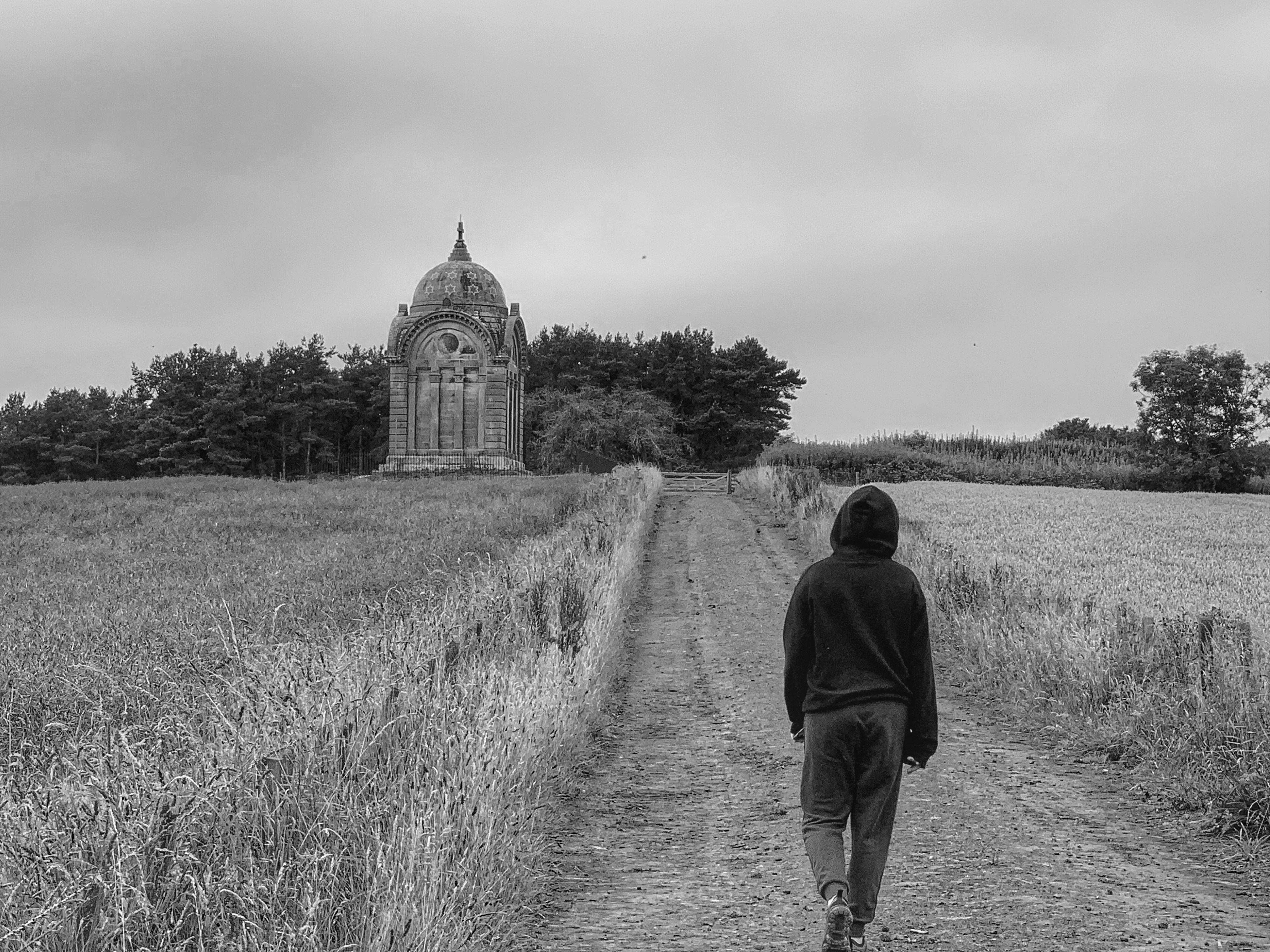man in black jacket walking on grass field in grayscale photography