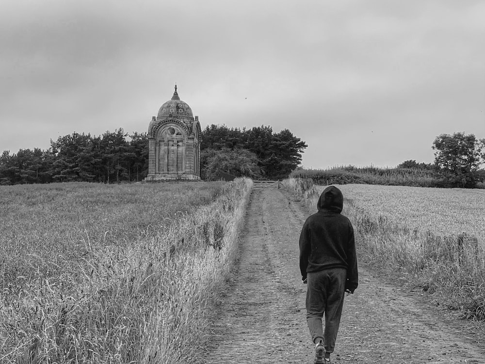 man in black jacket walking on grass field in grayscale photography