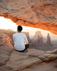 man in white shirt sitting on brown rock formation during daytime