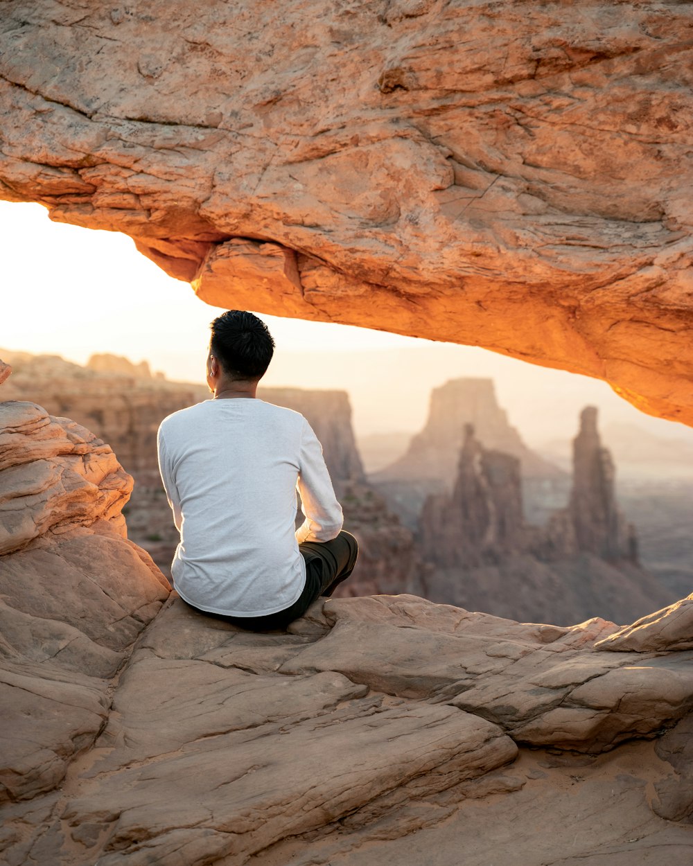 man in white shirt sitting on brown rock formation during daytime