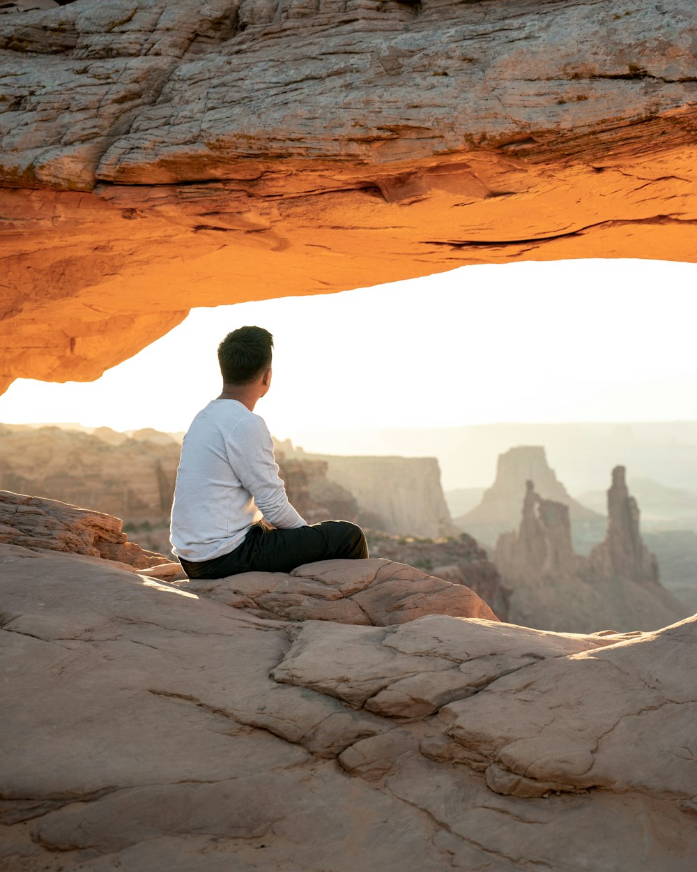 hombre en camisa blanca de manga larga sentado en la roca durante el día