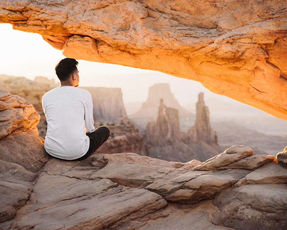 man in white long sleeve shirt sitting on rock during daytime