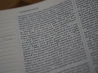 Close-up view of an open book with text, focusing on a passage related to a biblical story. The text is printed in a clear font, with some handwritten notes visible in the margins on lined paper. The page appears to be part of a religious scripture.