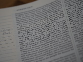 Close-up view of an open book with text, focusing on a passage related to a biblical story. The text is printed in a clear font, with some handwritten notes visible in the margins on lined paper. The page appears to be part of a religious scripture.