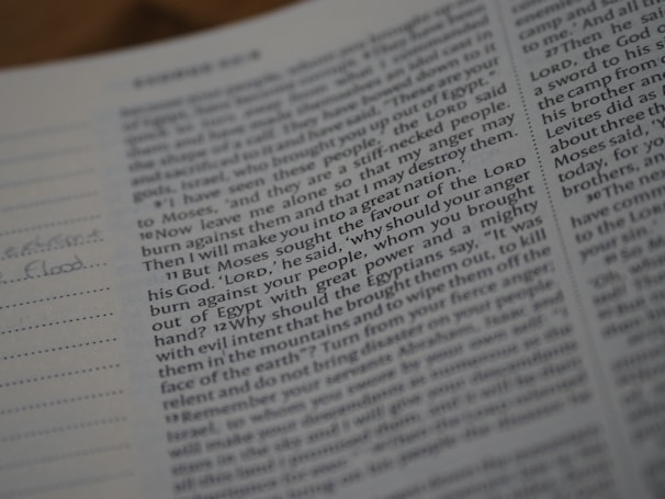 Close-up view of an open book with text, focusing on a passage related to a biblical story. The text is printed in a clear font, with some handwritten notes visible in the margins on lined paper. The page appears to be part of a religious scripture.