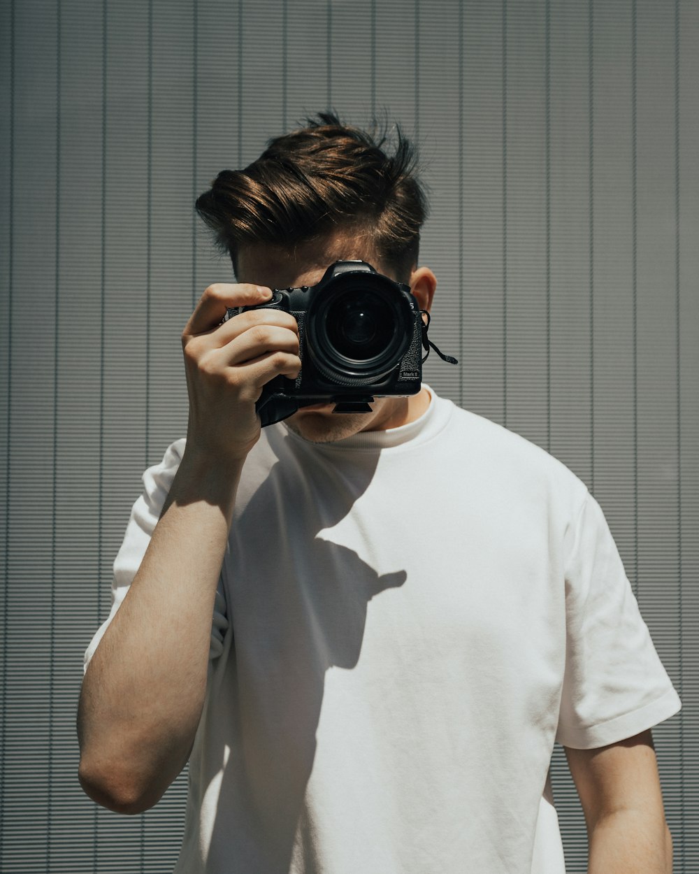 man in white crew neck t-shirt holding black nikon dslr camera