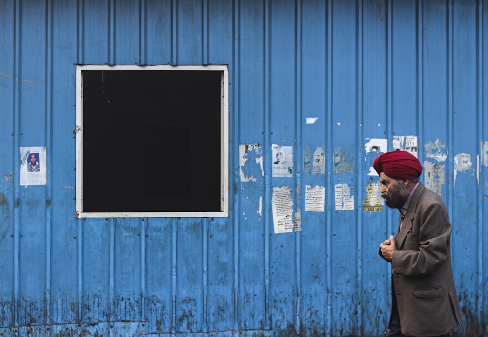 Mann mit roter Mütze steht neben blauer Holztür