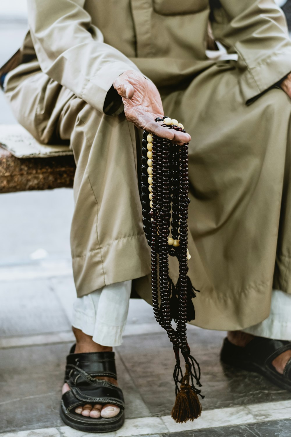 person in brown coat holding black beaded necklace