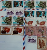 A collection of Vietnamese postage stamps is arranged on an envelope. The stamps feature a variety of designs, including flowers, historical figures, a rooster, a monument, and symbolic imagery. Some stamps include the Vietnamese flag and a portrait of a uniformed individual.