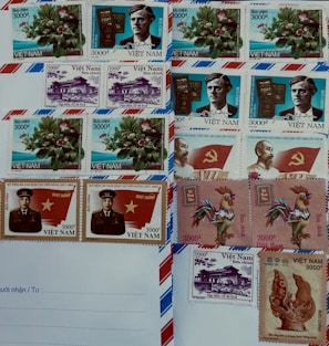 A collection of Vietnamese postage stamps is arranged on an envelope. The stamps feature a variety of designs, including flowers, historical figures, a rooster, a monument, and symbolic imagery. Some stamps include the Vietnamese flag and a portrait of a uniformed individual.
