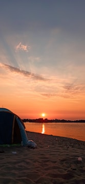 A spacious Luxtent set up on a serene beach at sunset, glowing warmly.
