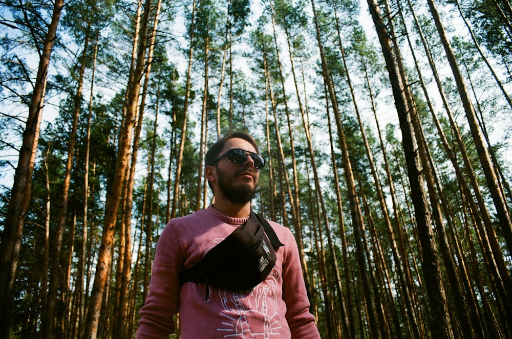 man in black sunglasses and brown jacket standing in the woods during daytime