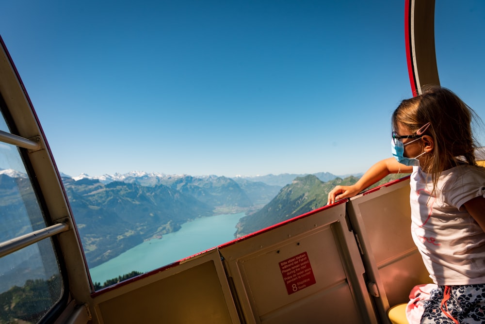 woman in black tank top sitting on brown wooden cabinet looking at snow covered mountains during