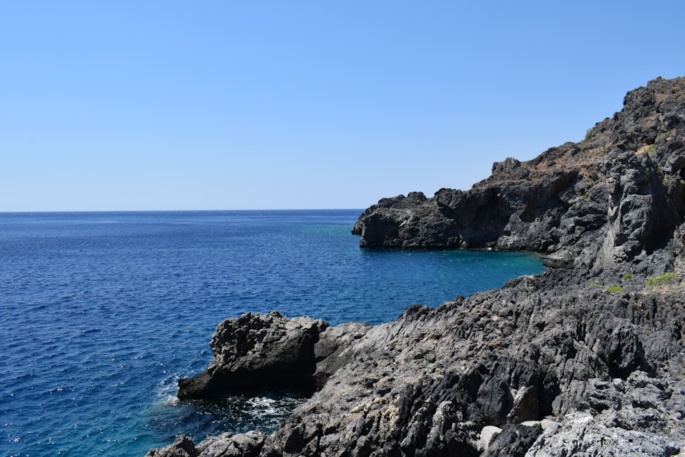 brown rocky mountain beside blue sea under blue sky during daytime