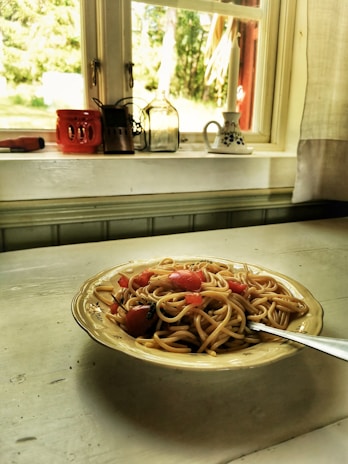 A warm kitchen bathed in golden hour sunlight with fresh avocados, herbs, and pasta laid out on a wooden bench.