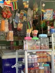 A vibrant store interior features an assortment of colorful packaged snacks and candy hanging from the ceiling. There are jars of lollipops and various nuts displayed on a glass shelf. The freezer at the bottom left corner has the word 'Ice' in white letters on a blue background.