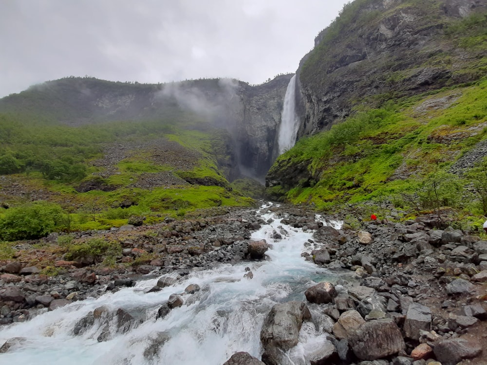 water falls between green grass covered mountain during daytime