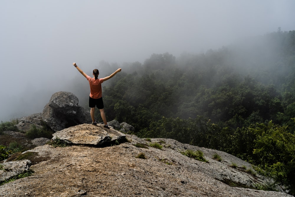 man in red shirt standing on rock formation during daytime