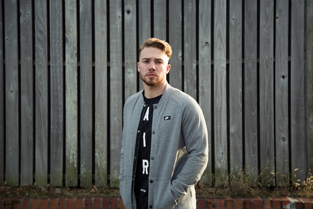 man in gray sweater standing near brown wooden fence