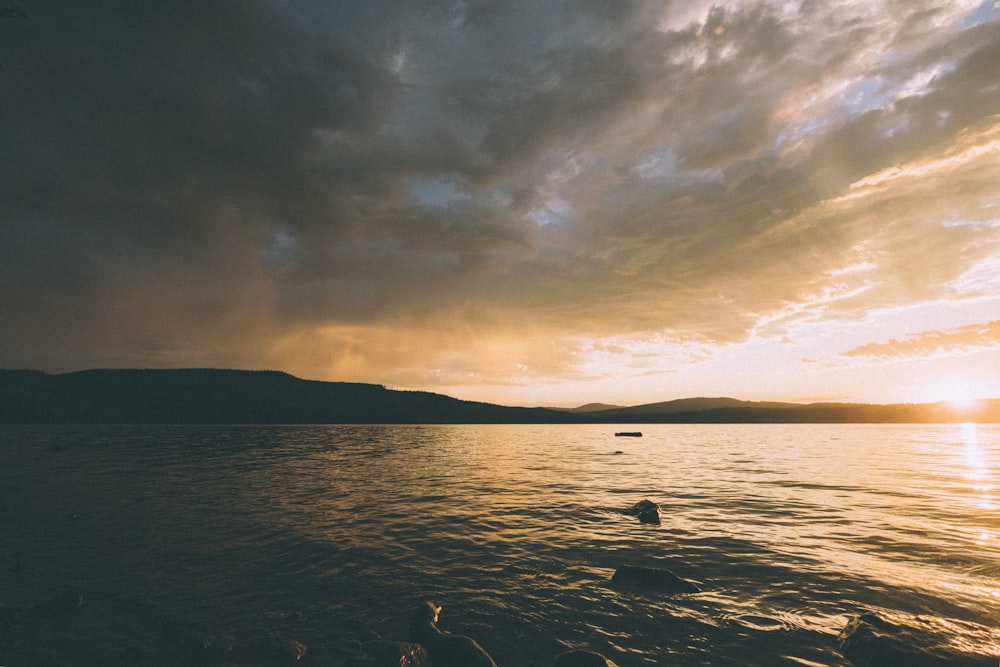 silhouette of 2 people on body of water during sunset